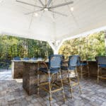 A brick patio with blue chairs and a ceiling fan.
