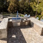 An outdoor kitchen with a grill and chairs.