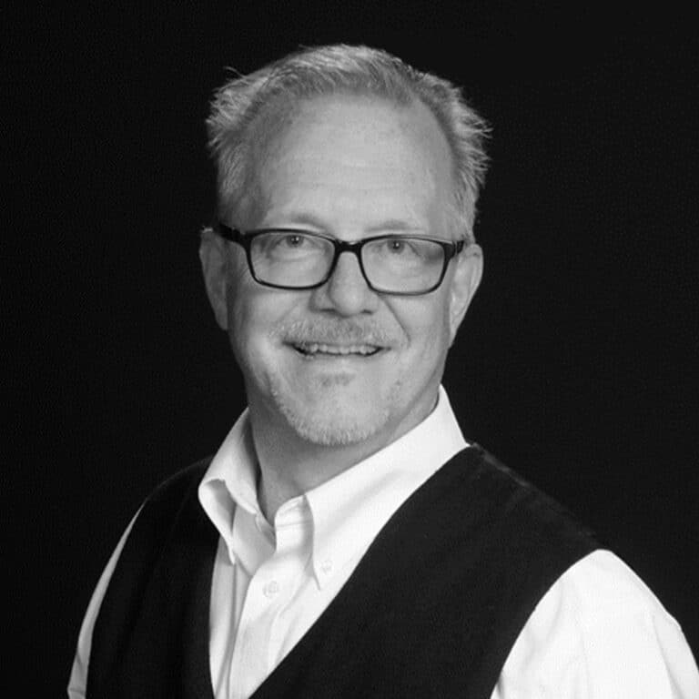 A black and white photo of a man wearing glasses and a vest.